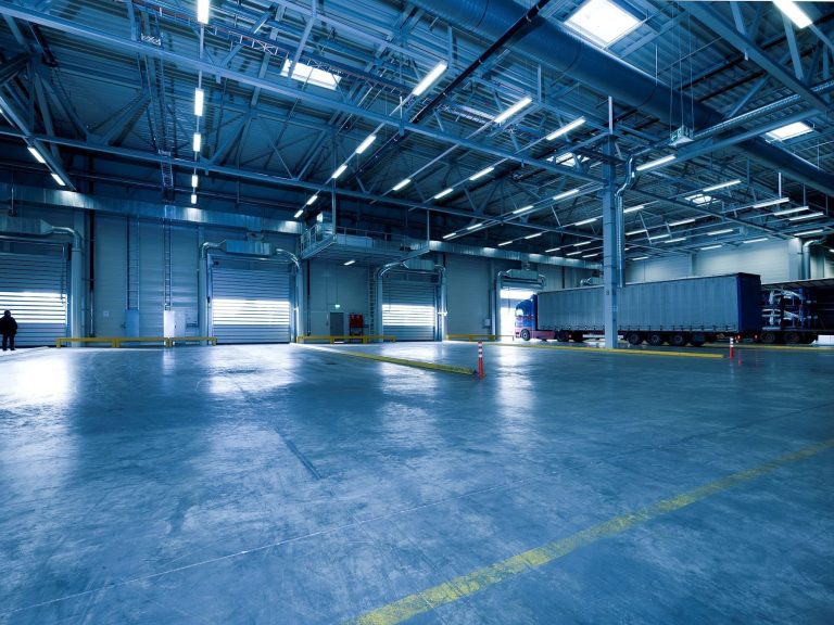 Lagerhallen als Beispiel für ein Nichtwohngebäude Helle Lagerhalle mit Betonboden und großen Fenstern, Lkw-Anhänger am Dock. Nichtwohngebäude.